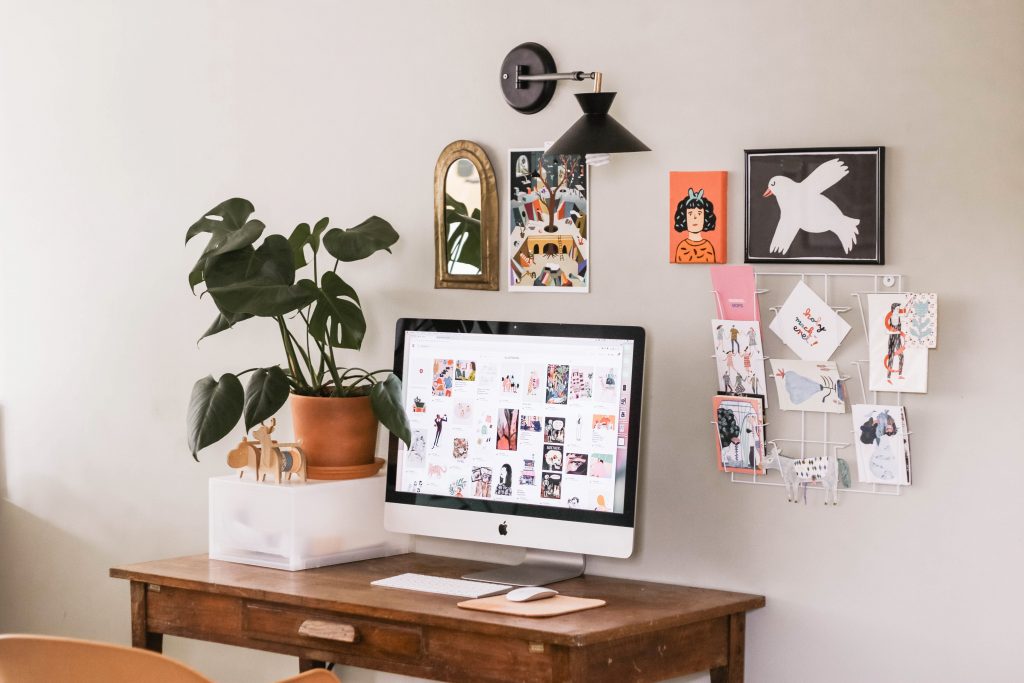 desk with desktop computer, potted plant, and pictures and posters on the wall